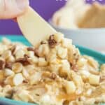 A dip topped with caramel, apples, white chocolate chips, and pecans scooped up on an apple slice with text overlay that says "Caramel Apple Hummus".