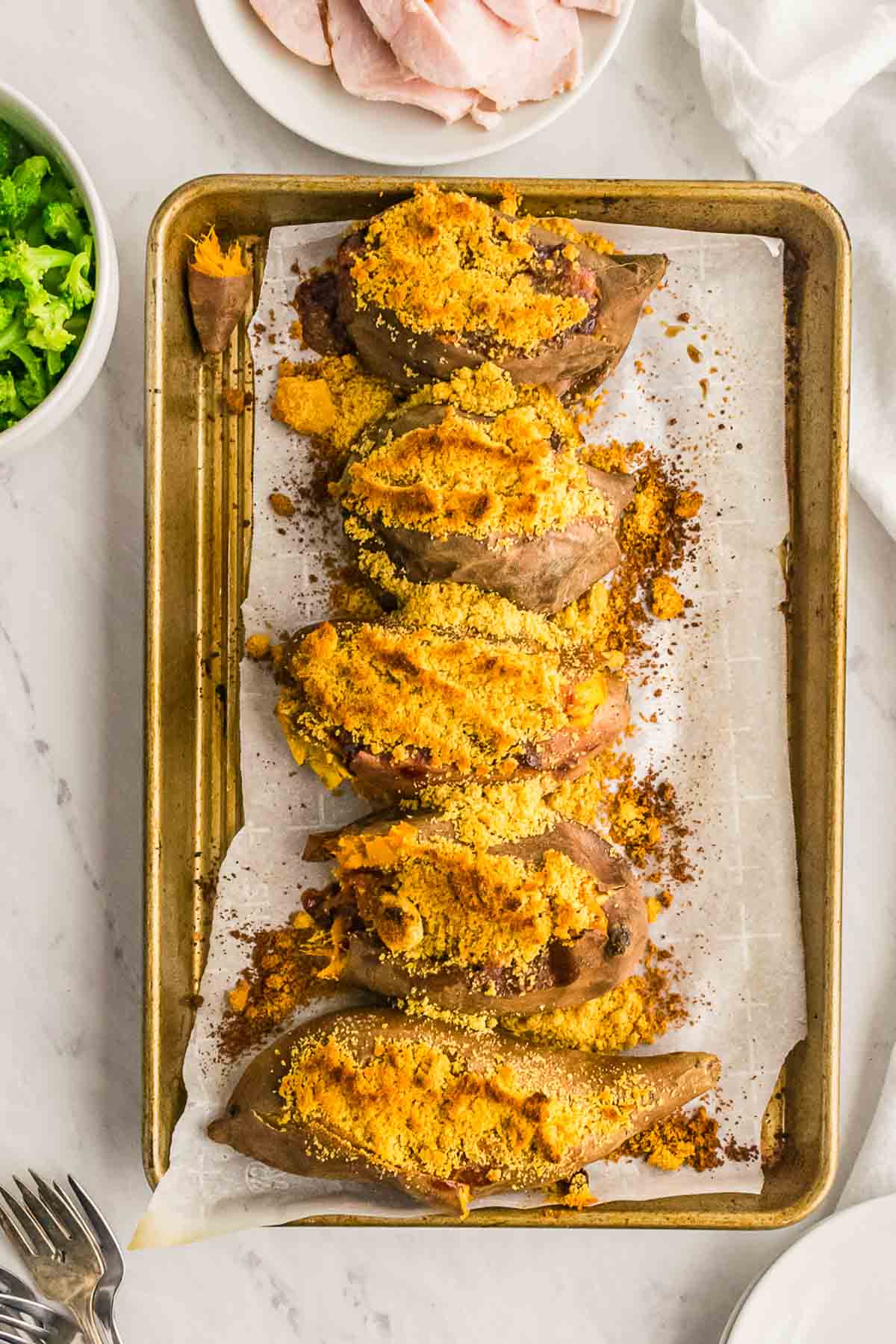Five crumb-topped stuffed sweet potatoes on a sheet pan.