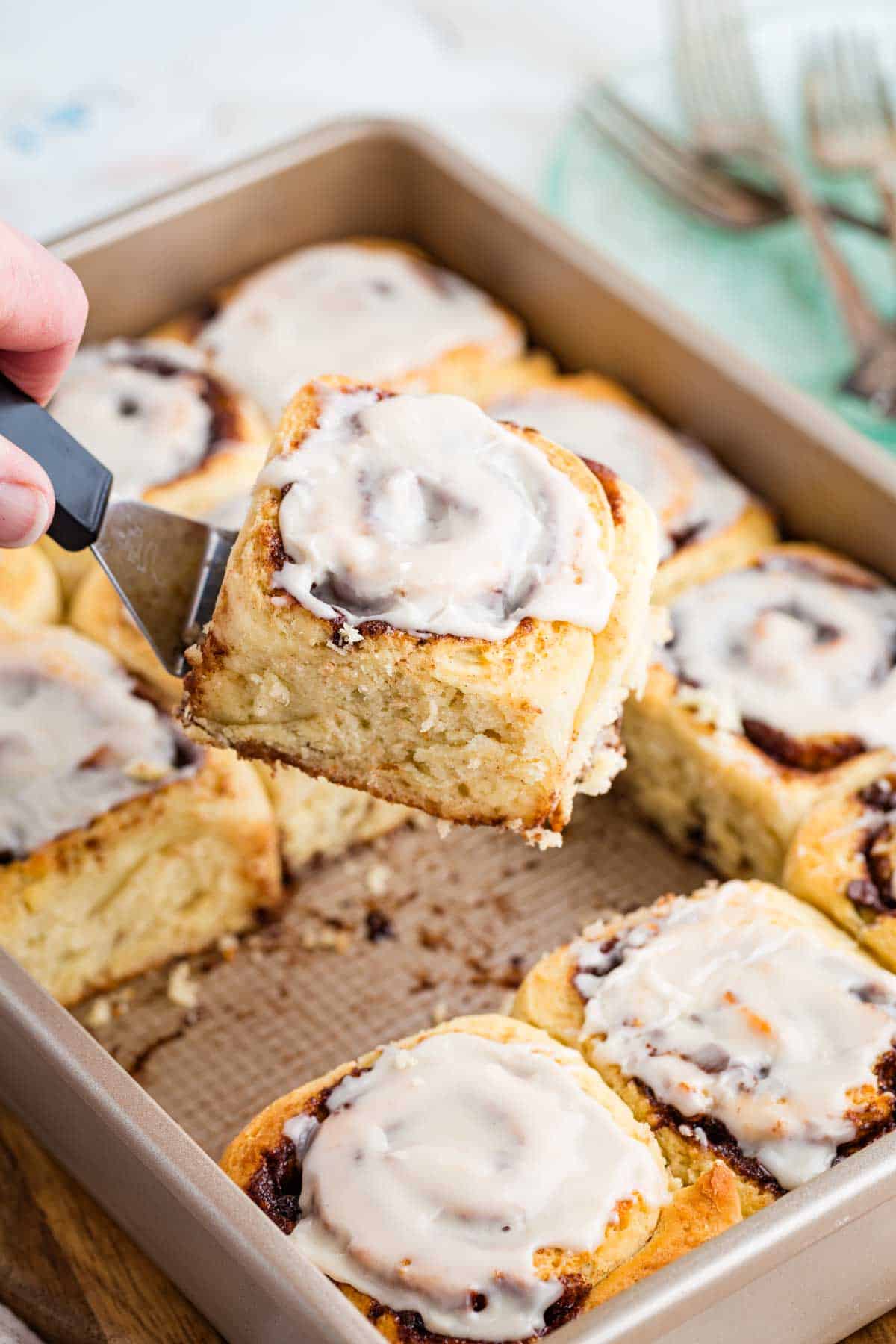 A spatula lifting a gluten-free chocolate cinnamon roll out of a baking pan.