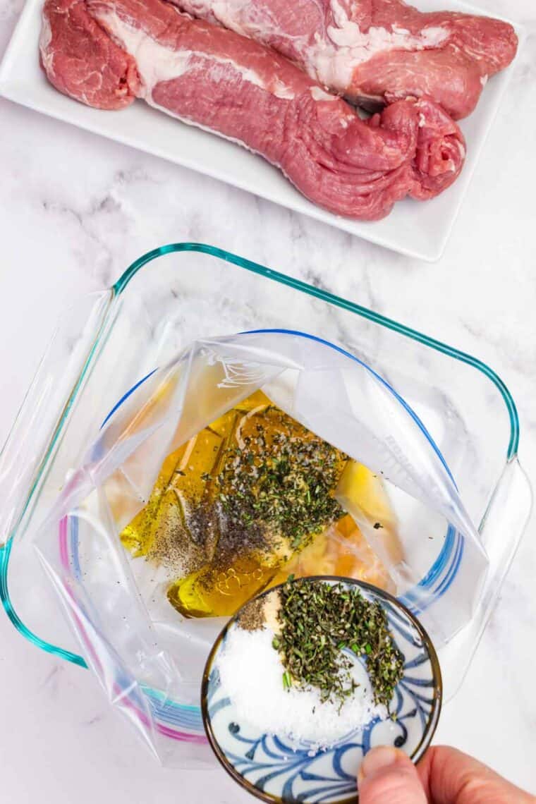 Adding seasonings and herbs to a marinade for bourbon pork tenderloin in a ziplock bag.