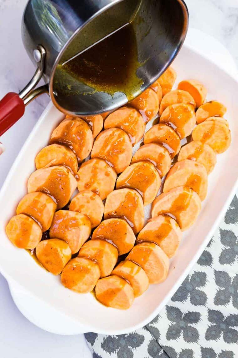 Pouring brown sugar glaze over sweet potato slices arranged in a baking dish.