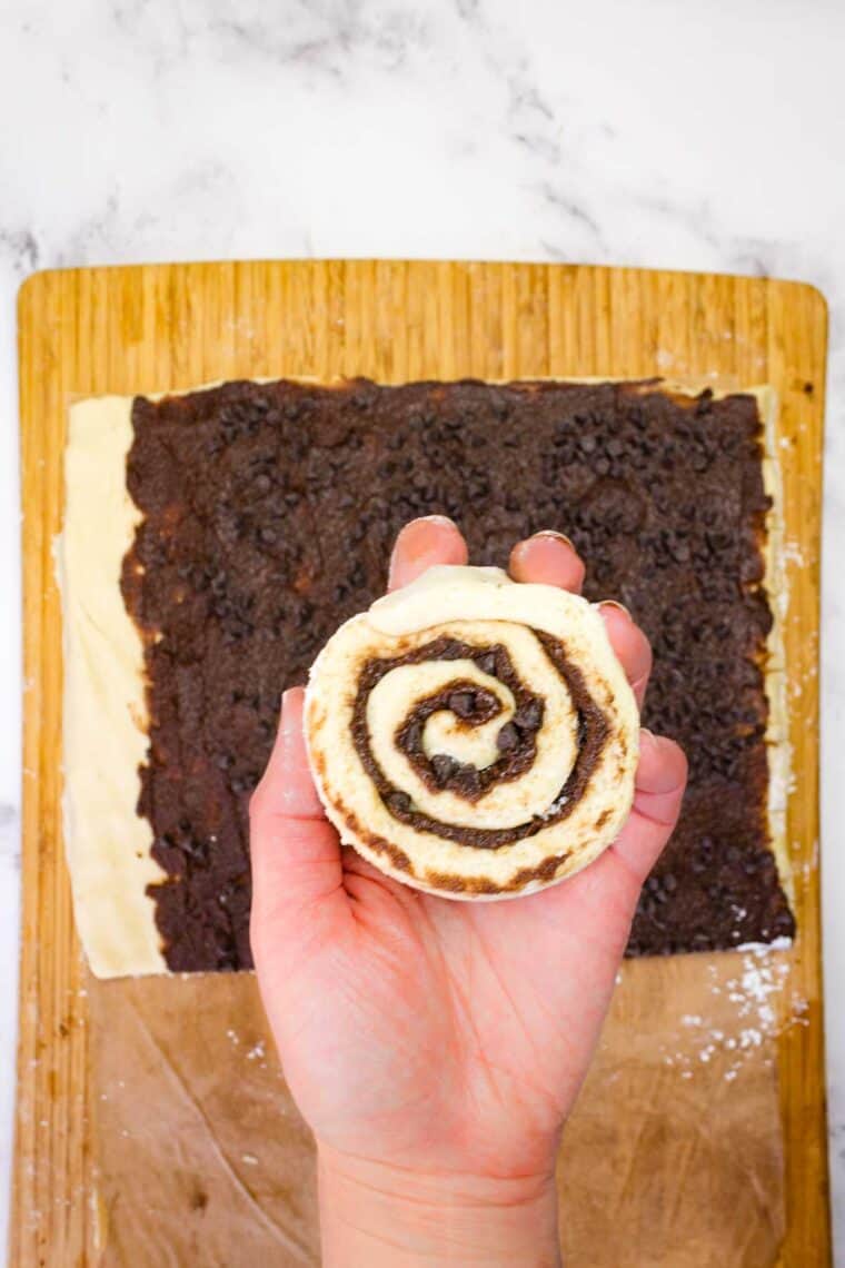 A hand holding an unbaked gluten-free chocolate cinnamon roll up to the camera.