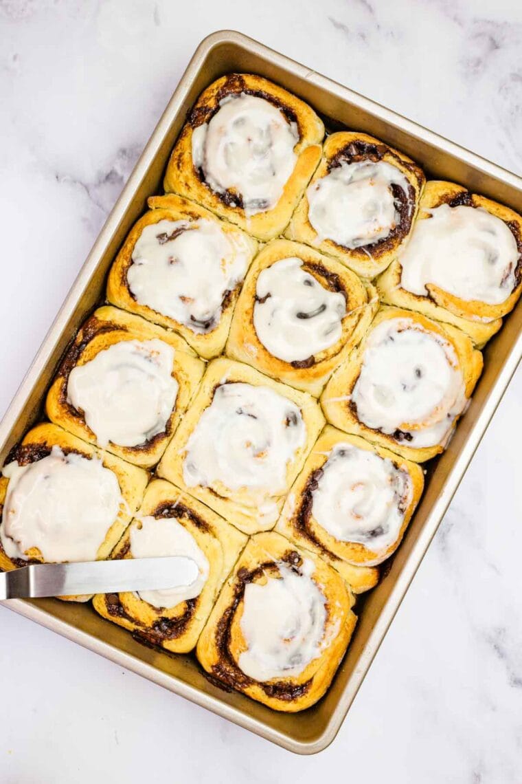 Spreading vanilla glaze over warm gluten-free chocolate cinnamon rolls.