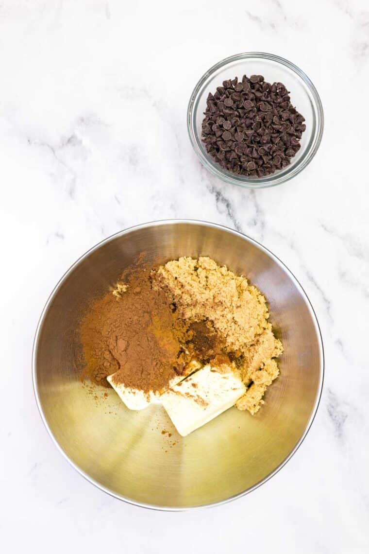 Butter, brown sugar, cocoa powder, cinnamon, and vanilla in a bowl near a bowl of mini chocolate chips.