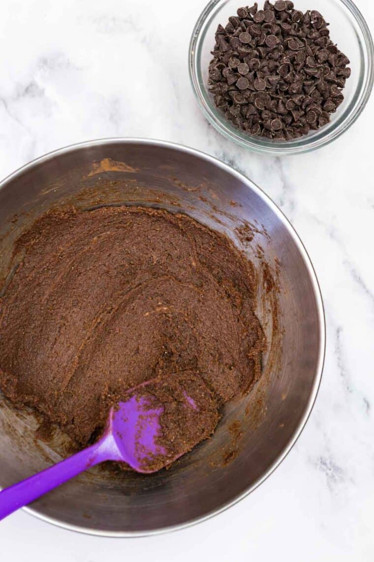 Butter, brown sugar, cocoa powder, cinnamon, and vanilla mixed together in a bowl near a bowl of mini chocolate chips.
