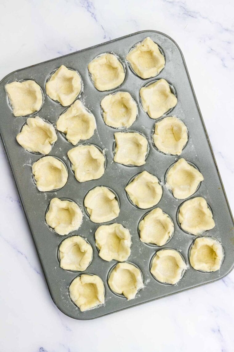Crescent roll dough pressing into a cupcake tins.