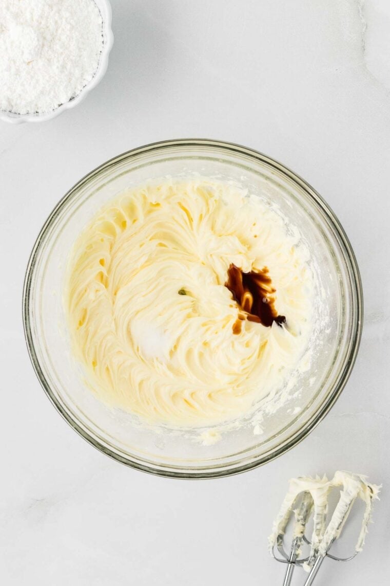 Adding vanilla and salt to creamed butter and powdered sugar.