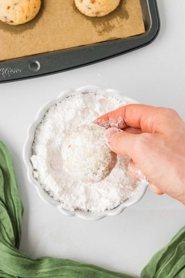 Rolling a toffee almond snowball cookie in powdered sugar.