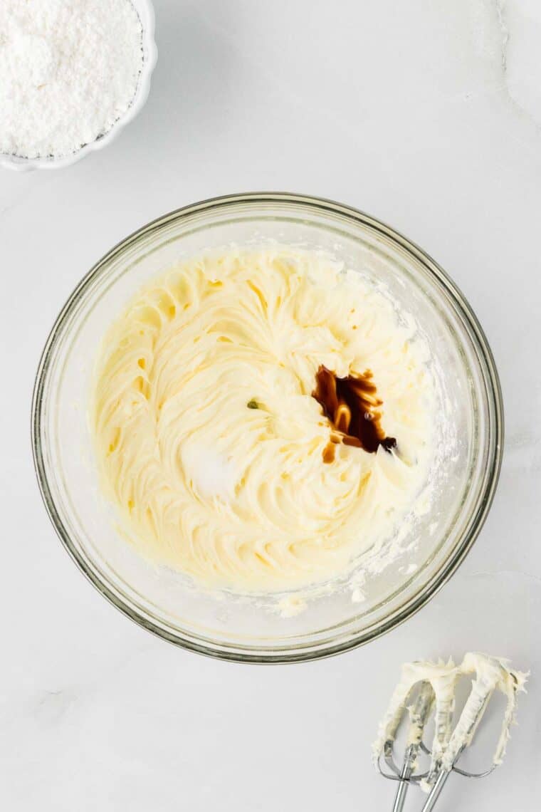 Adding vanilla and salt to creamed butter and powdered sugar.