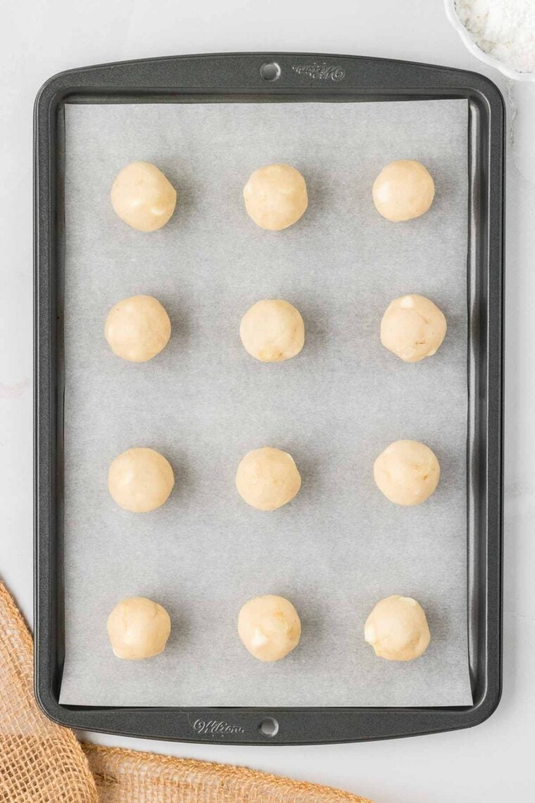 Balls of white chocolate macadamia snowball cookie dough on a baking sheet.