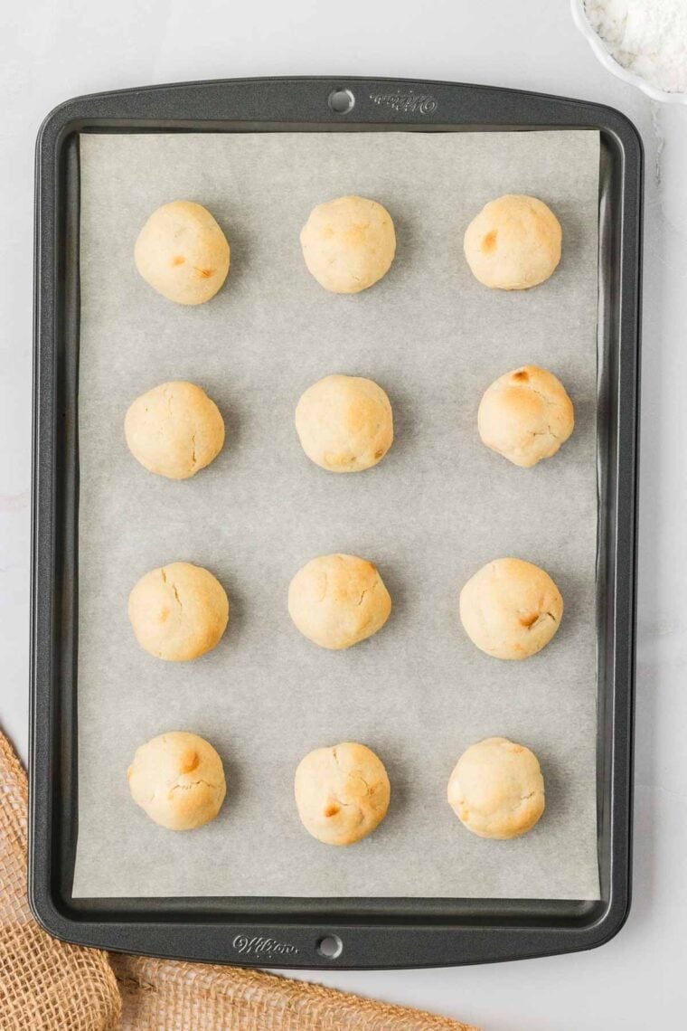 Baked balls of white chocolate macadamia snowball cookie dough on a baking sheet.