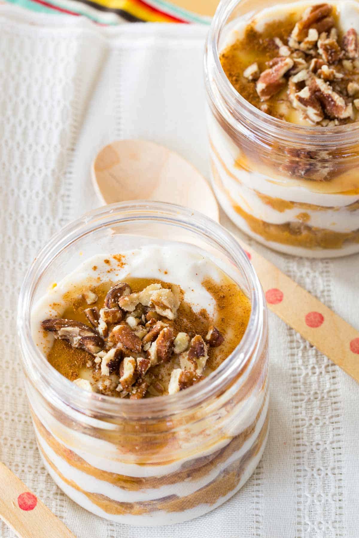 Two pumpkin pie Greek yogurt parfaits on top of a lacy cloth napkin.