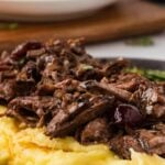 Shredded beef on top of mashed potatoes with text overlay that says "Slow Cooker Cranberry Balsamic Beef".