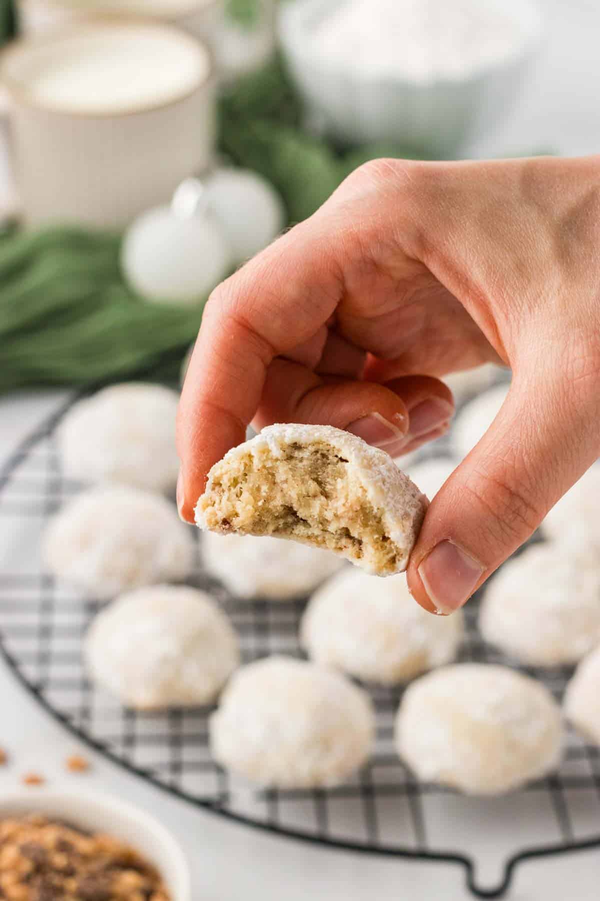 A hand holding a toffee almond snowball (with a bit taken out of it) up to the camera.