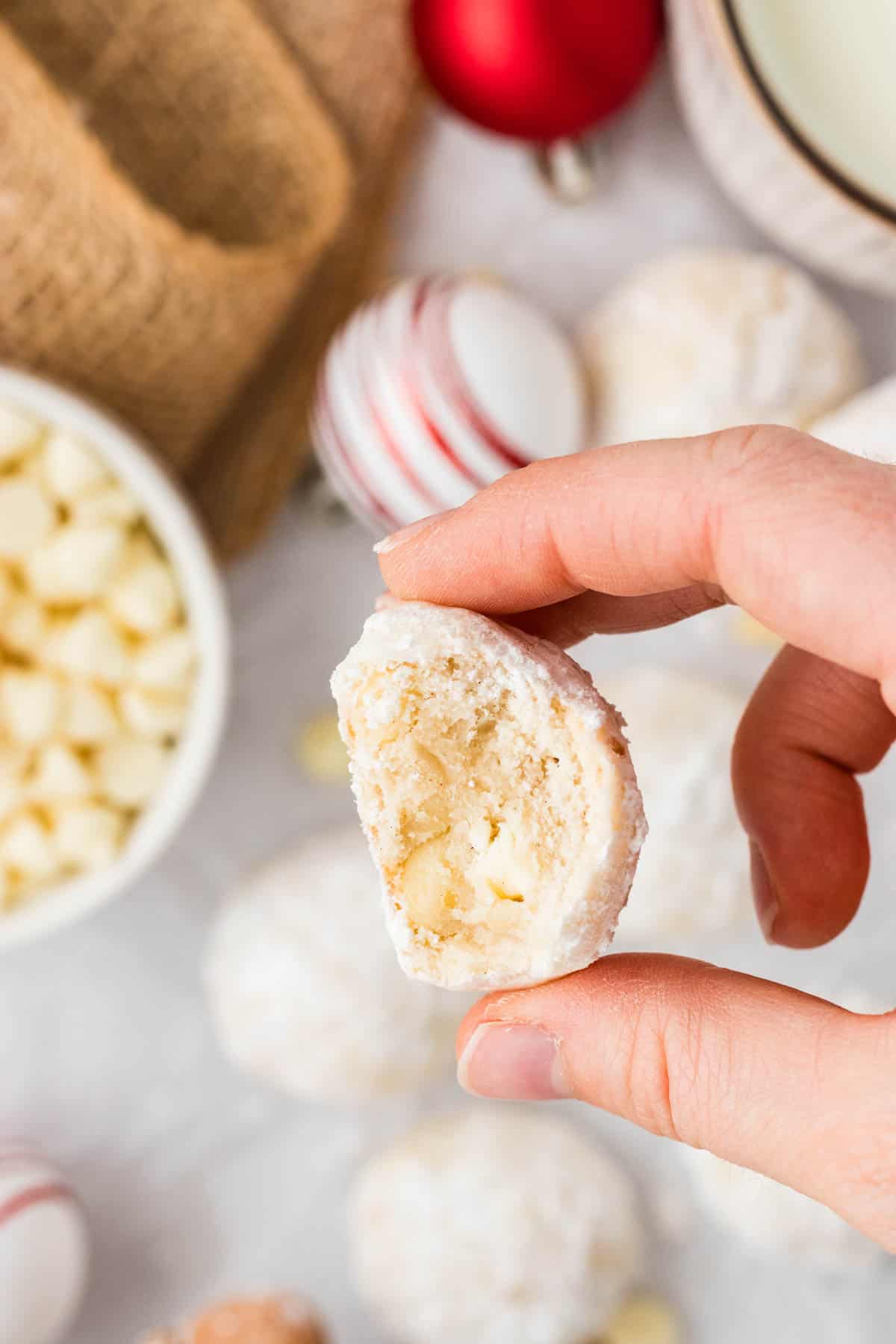 A hand holding a gluten-free white chocolate macadamia snowball cookie up to the camera.