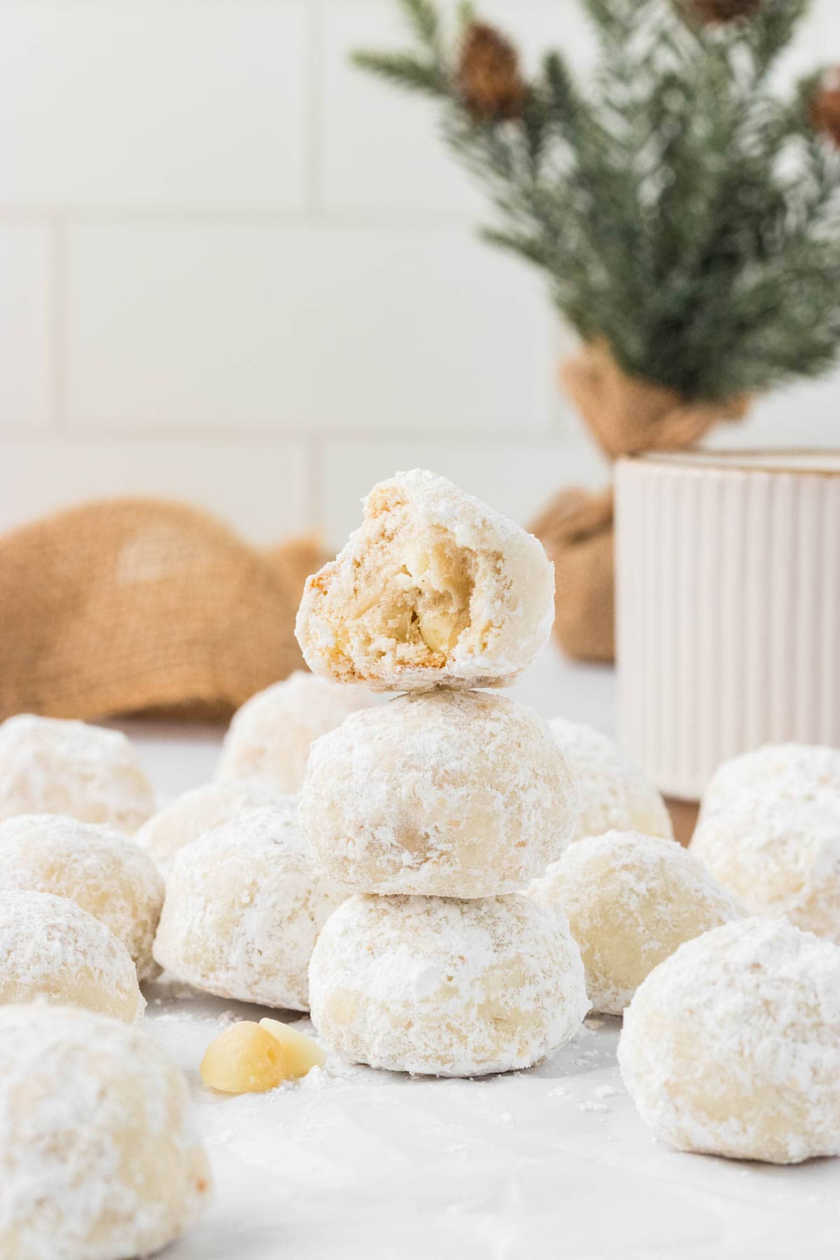 A stack of white chocolate macadamia snowball cookies. The top one has a bite taken out of it.