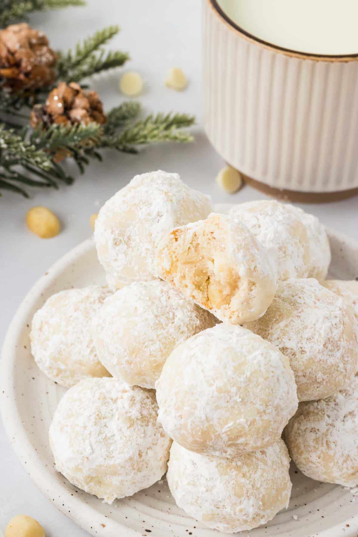 A pile of white chocolate macadamia snowball cookies. One has a bite taken out of it.