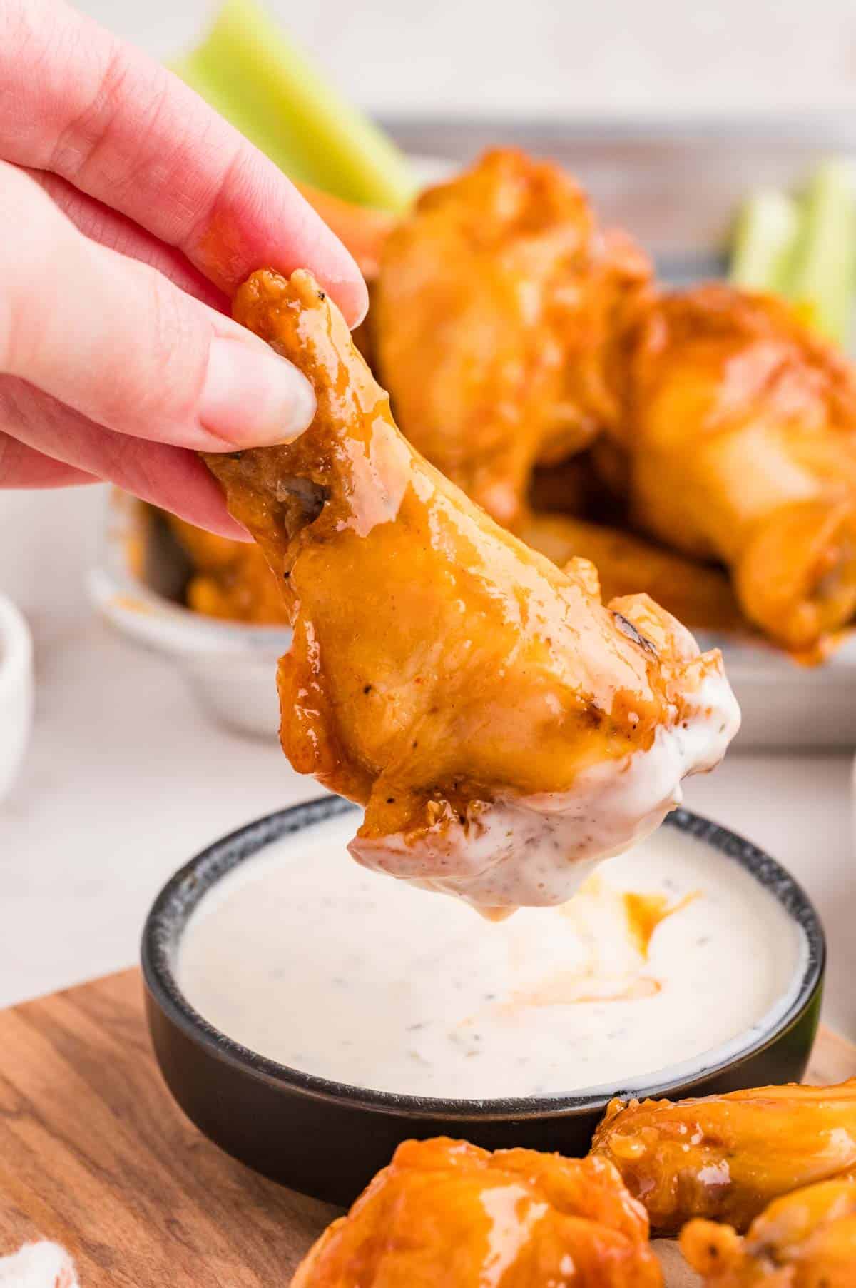 A hand dipping a baked buffalo wing in ranch dressing