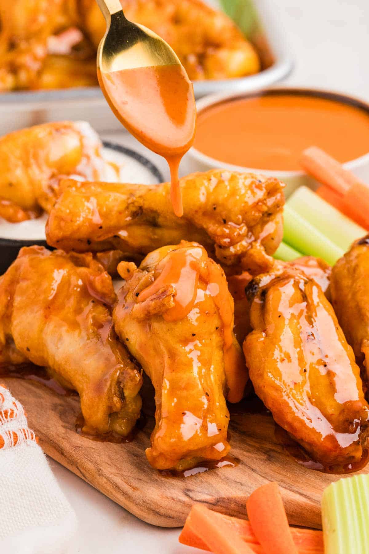 Drizzling buffalo sauce over baked buffalo wings on a wooden baking sheet
