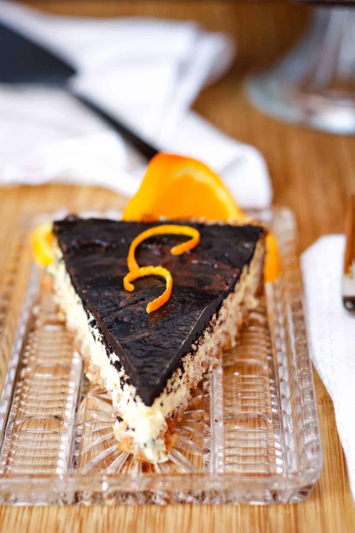 Orange ricotta tart with almond crust, topped with a glossy dark chocolate glaze and garnished with orange zest.