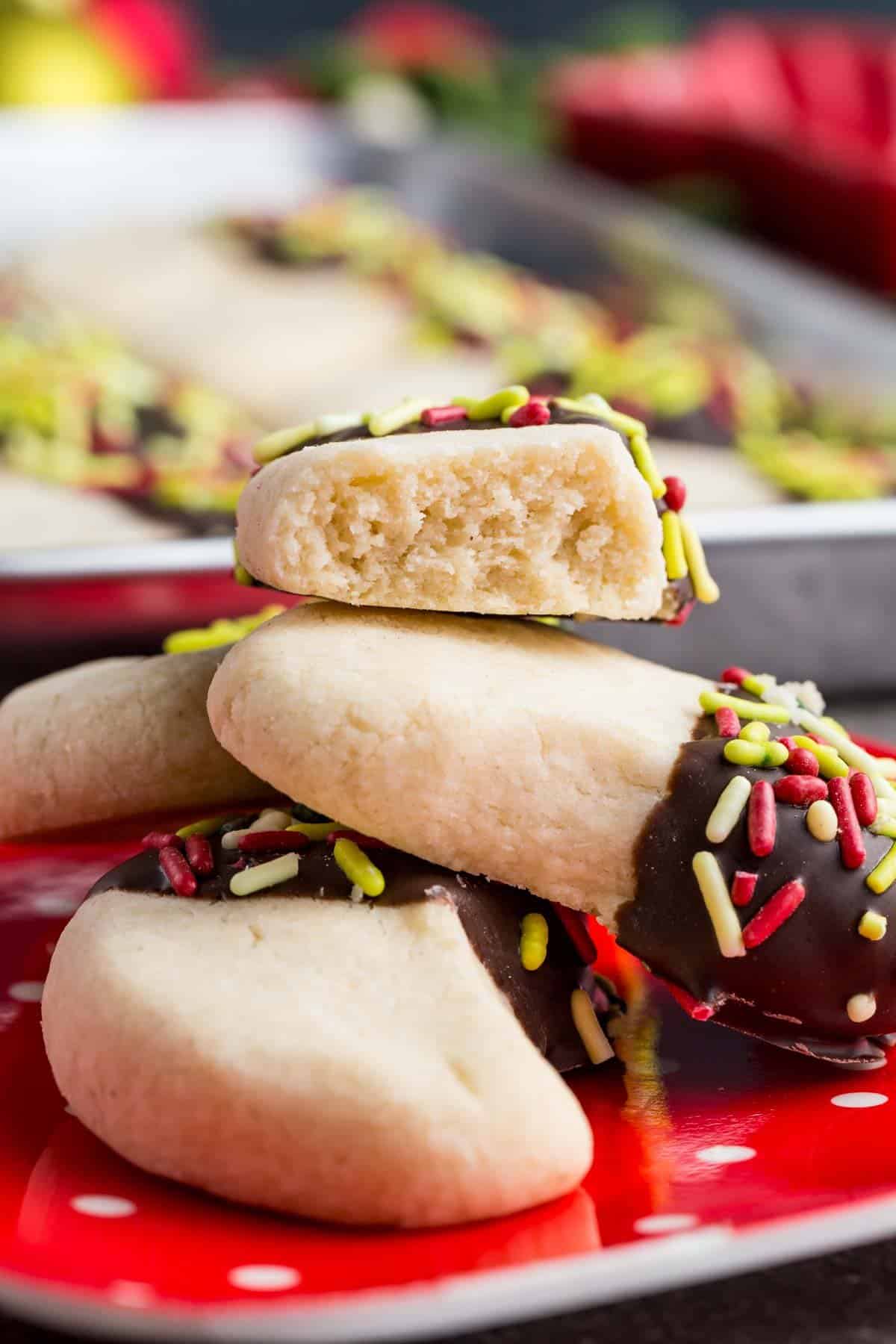 Make tender, buttery gluten-free almond crescent cookies dipped in chocolate! They're the easiest Christmas cookies with only 4 ingredients. A few almond crescent piled up with the one on top broken in half.