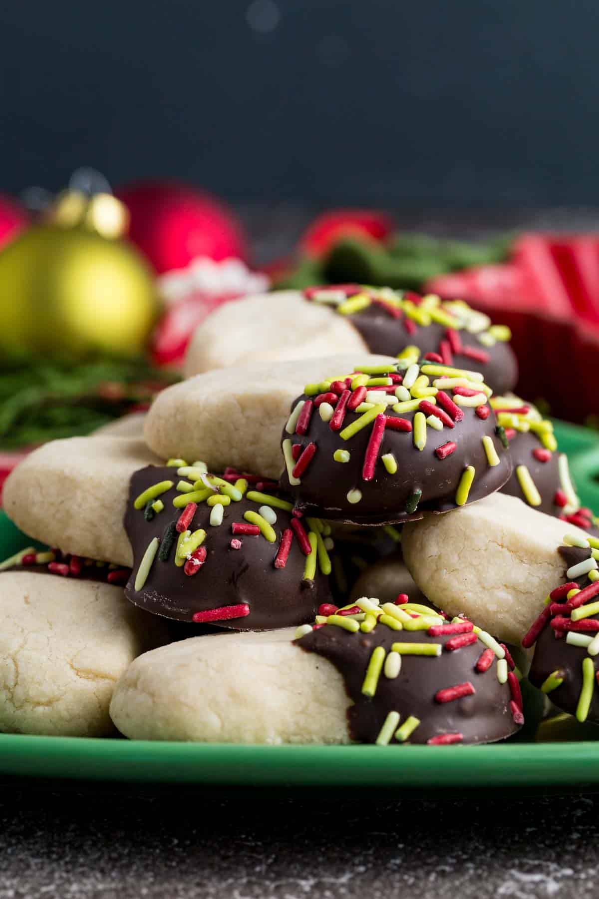 Make tender, buttery gluten-free almond crescent cookies dipped in chocolate! They're the easiest Christmas cookies with only 4 ingredients. A closeup of a pile of almond crescent cookies with one end dipped in chocolate and sprinkles.