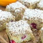 Pieces of gluten free cranberry cake on a cutting board with an orange, cinnamon sticks, and fresh cranberries around them.