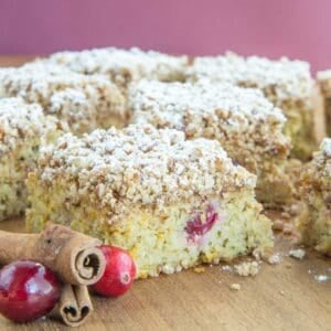 Slices of cranberry coffee cake on a cutting board with a couple of cinnamon sticks and fresh cranberries.
