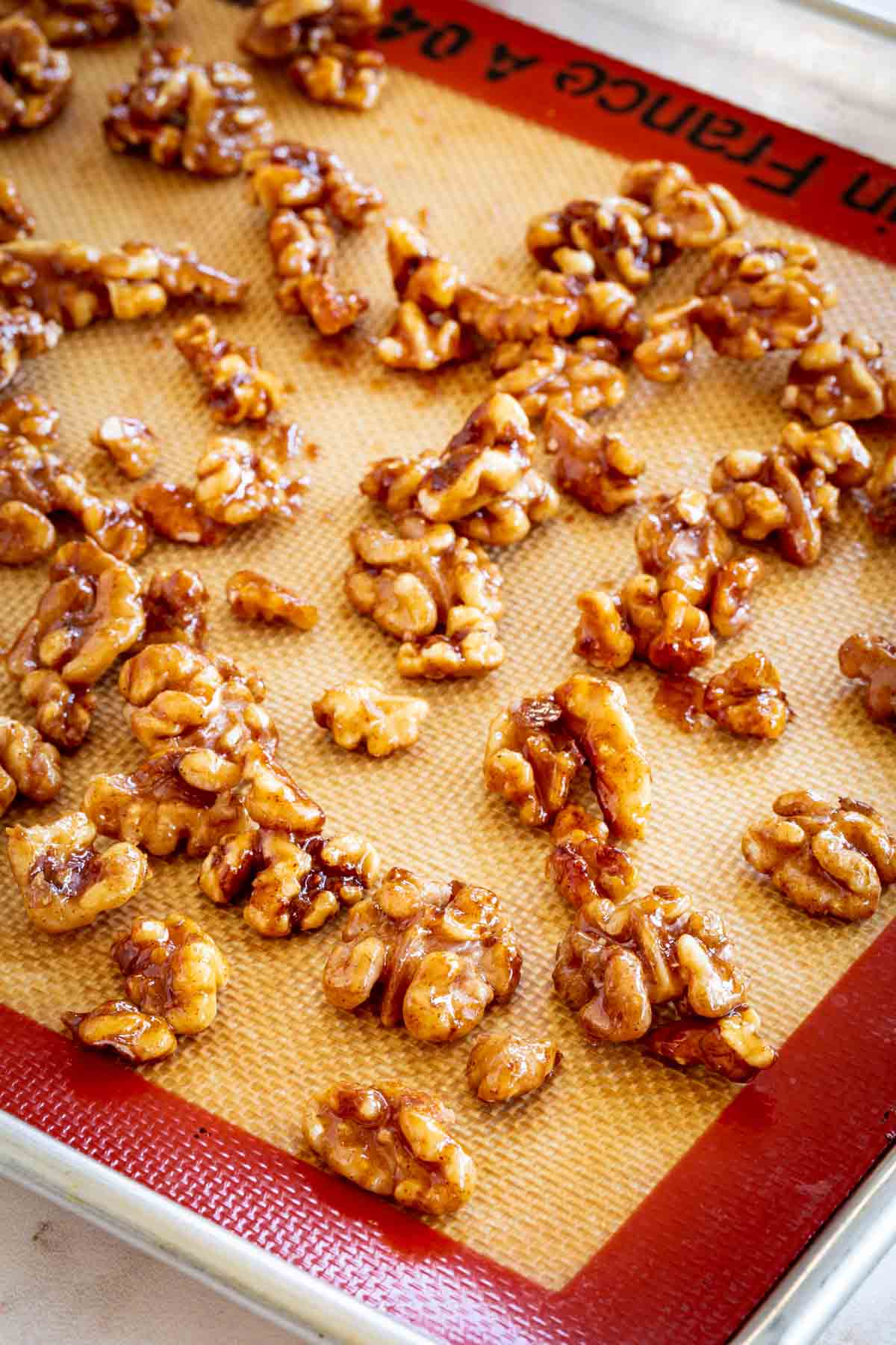 Honey glazed walnuts spread out on a silicone baking mat.