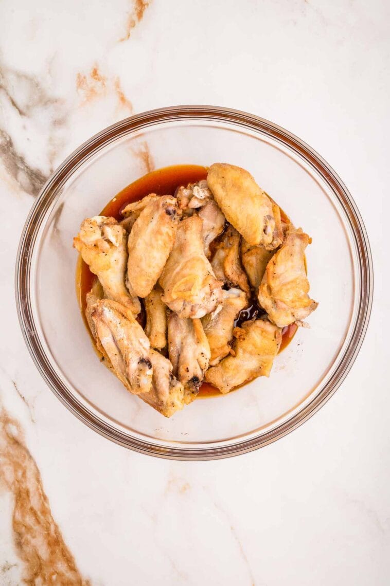 Baked wings and buffalo wing sauce in a glass bowl