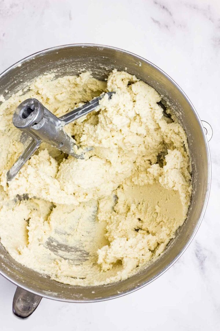 Almond crescent cookie dough in a mixing bowl with the paddle attachment resting in there.