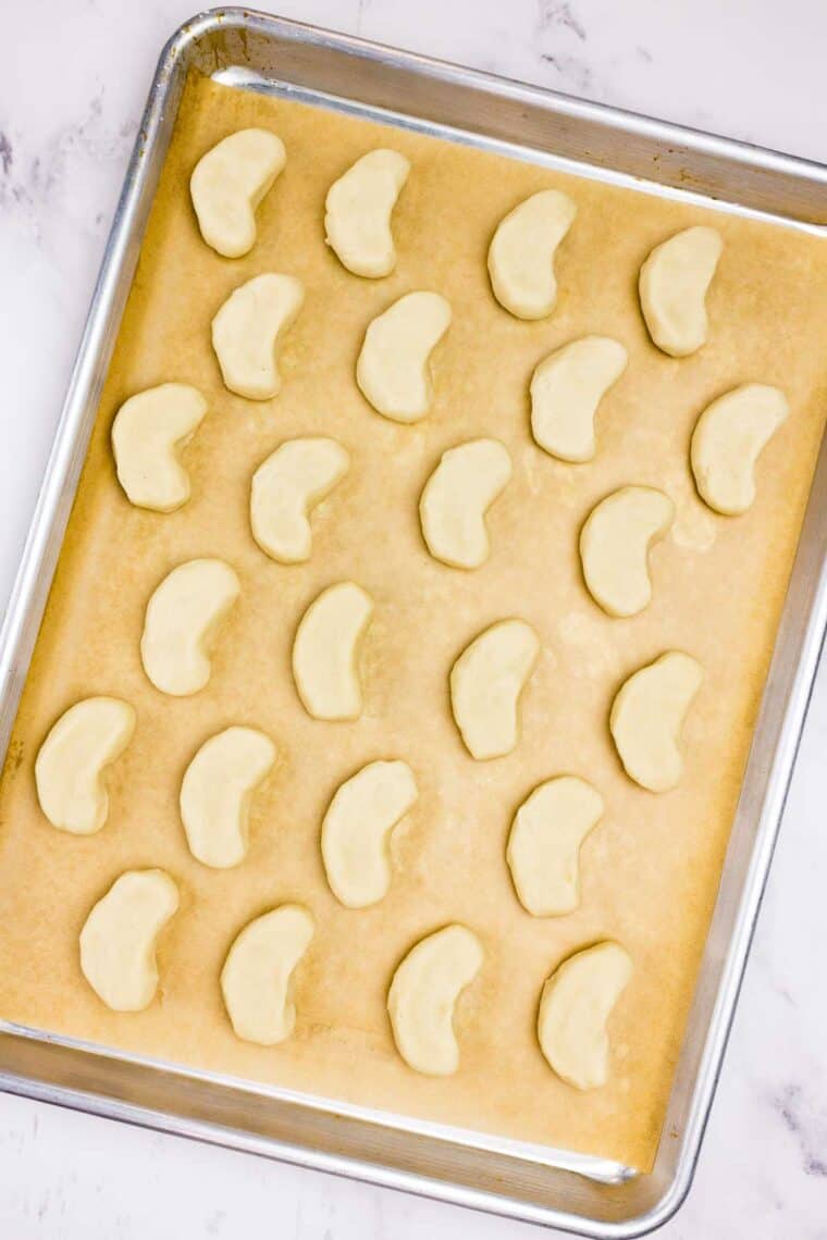 Cookie dough shaped into crescents on a parchment lined baking sheet.