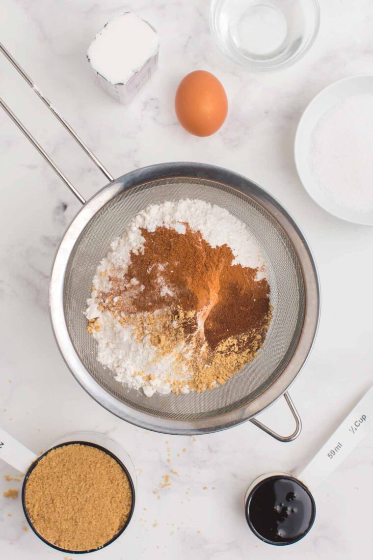 Flour and spices in a sifter over a bowl.