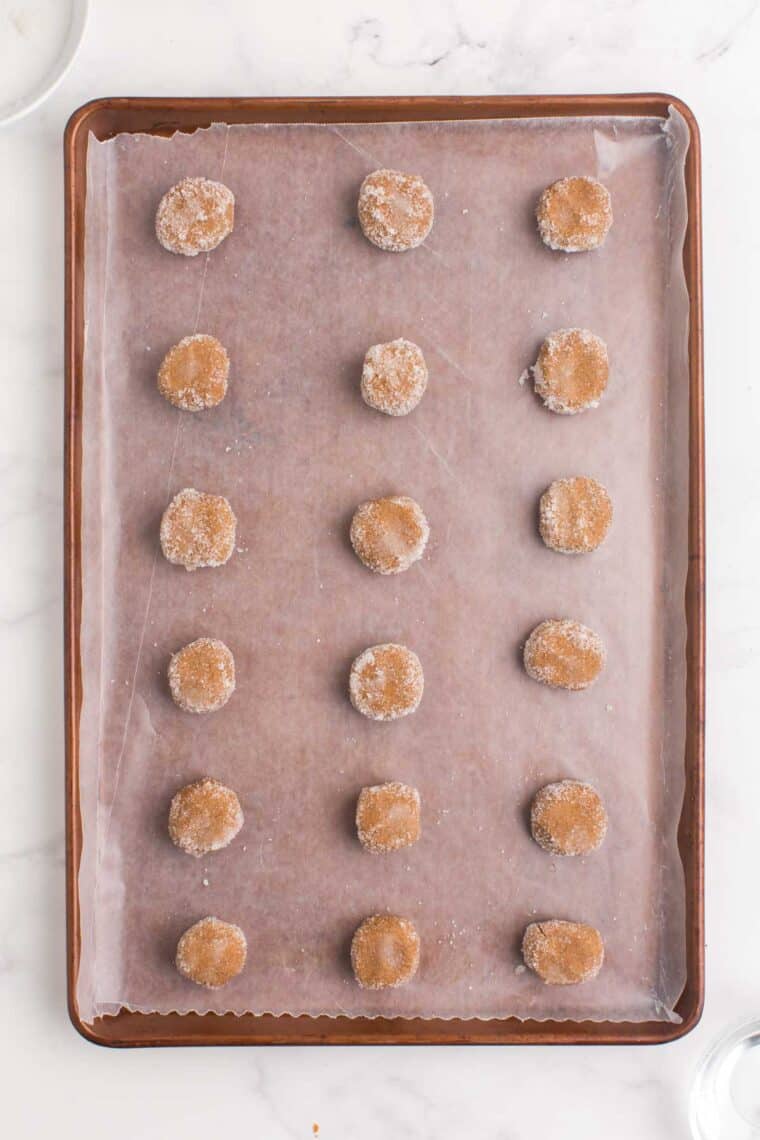Balls of cookie dough ball rolled in sugar on a sheet pan.