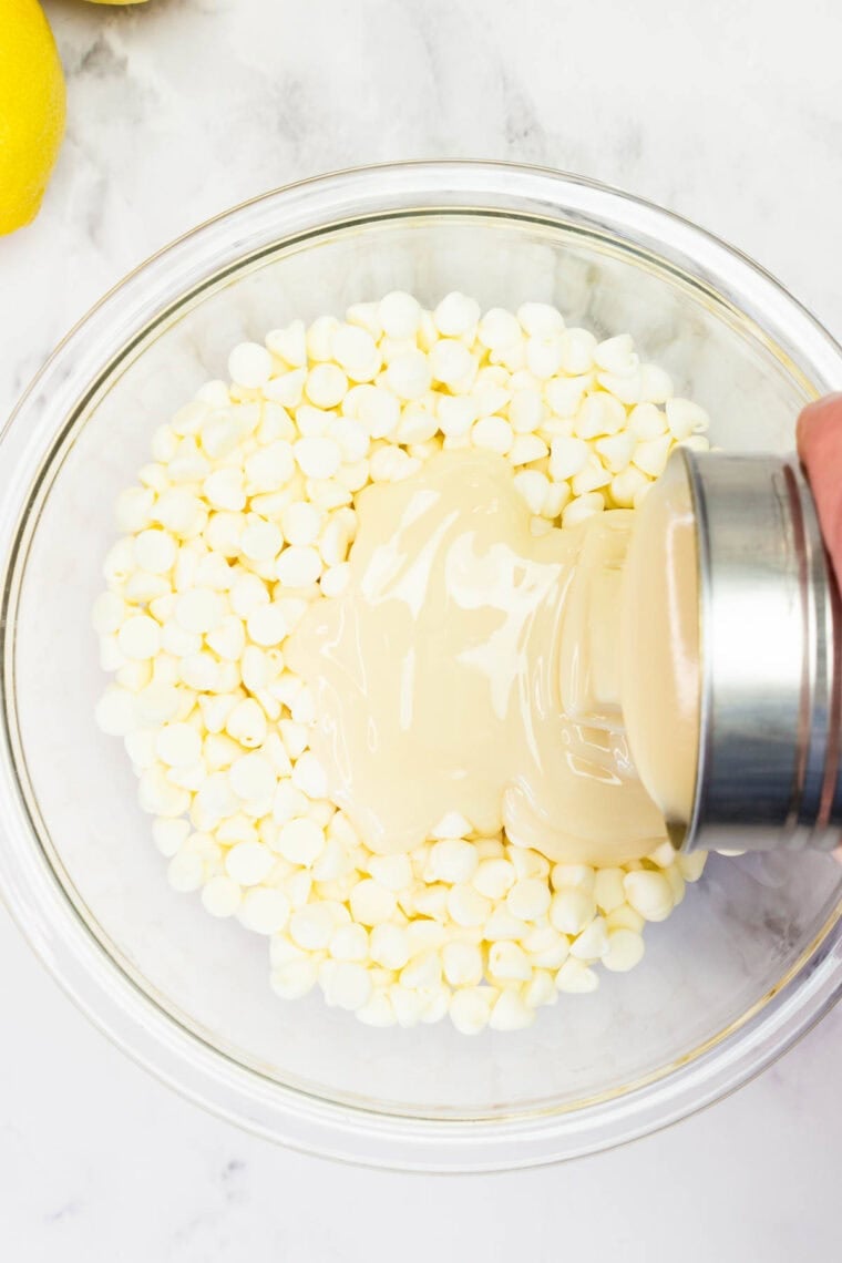 Pouring sweetened condensed milk over white chocolate chips
