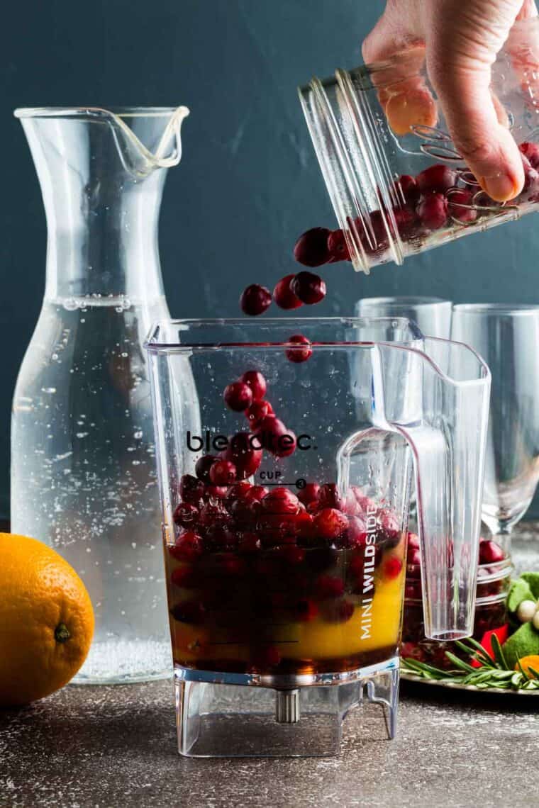 Fresh cranberries being poured into a blender with orange juice.