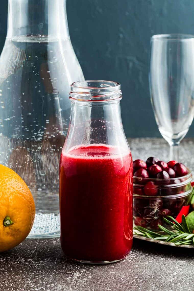 Fresh cranberry juice in a bottle with a bottle of club soda behind it.