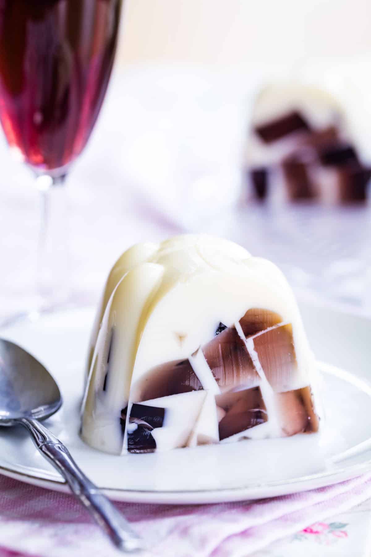 A slice of vanilla ice cream jello mold with purple sparkling cider gelatin cubes floating in it on a white plate.