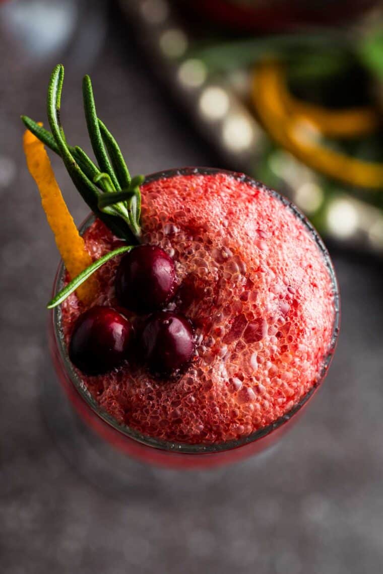 Cranberries, orange zest, and a rosemary sprig on top of the bubbles in a flute glass.