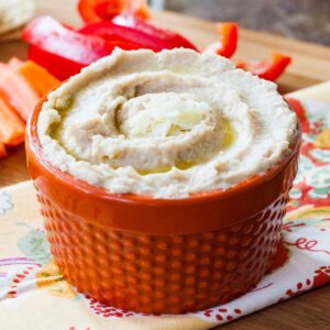 Truffle white bean hummus garnished with shaved parmesan in an orange bowl.
