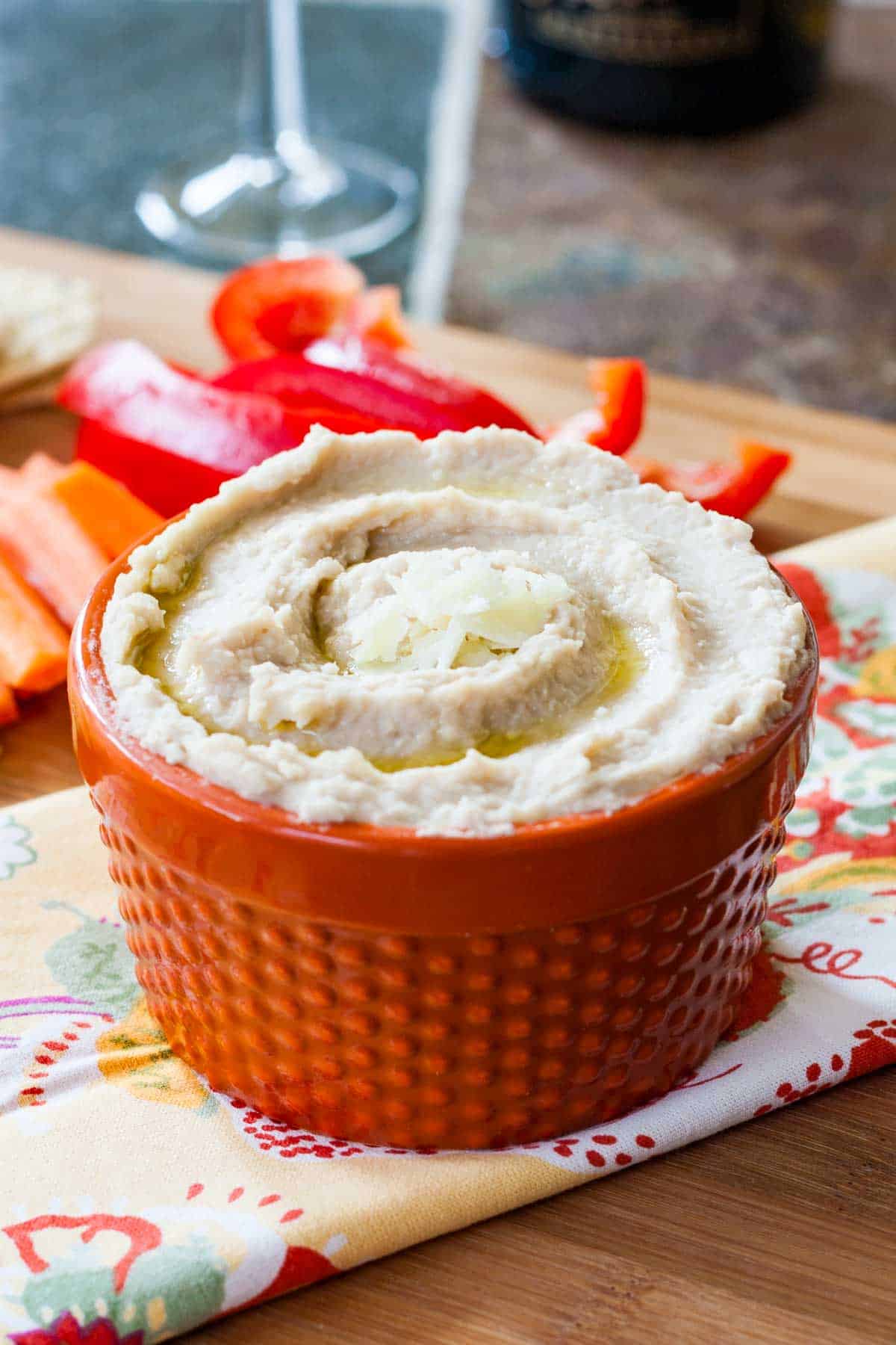 An orange bowl of hummus topped with truffle oil and parmesan cheese.