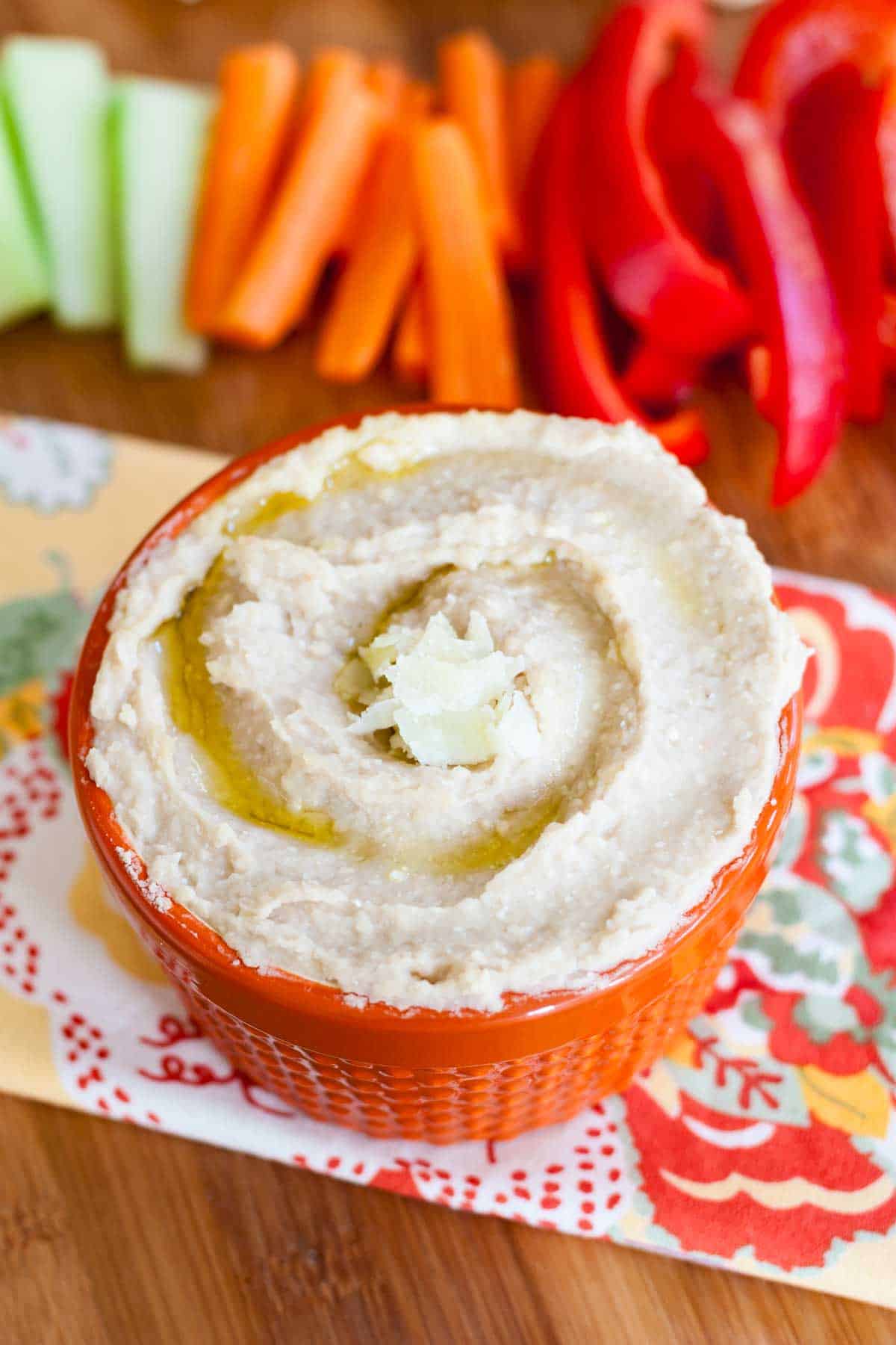 White bean dip in an orange bowl with a drizzle of oil and parmesan flakes on top.