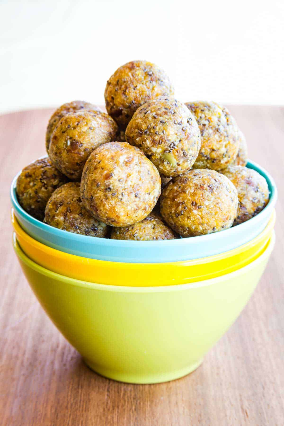 Three stacked colorful bowls filled with apricot energy balls.