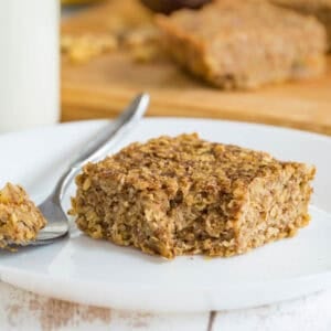 A banana breakfast bar on a plate with a corner cut off on a fork next to it.