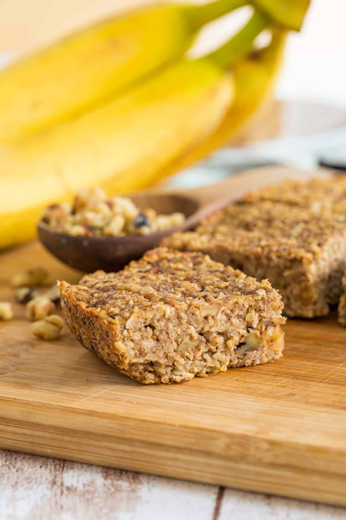 A breakfast bar on a cutting board with bananas and chopped walnuts in the background.