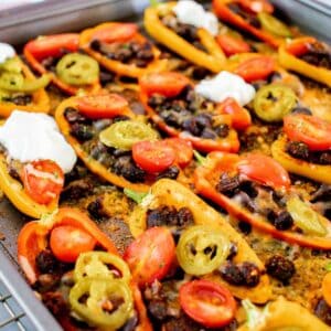 Mini bell pepper nachos filled with black beans, cheese, and other toppings on a sheet pan.