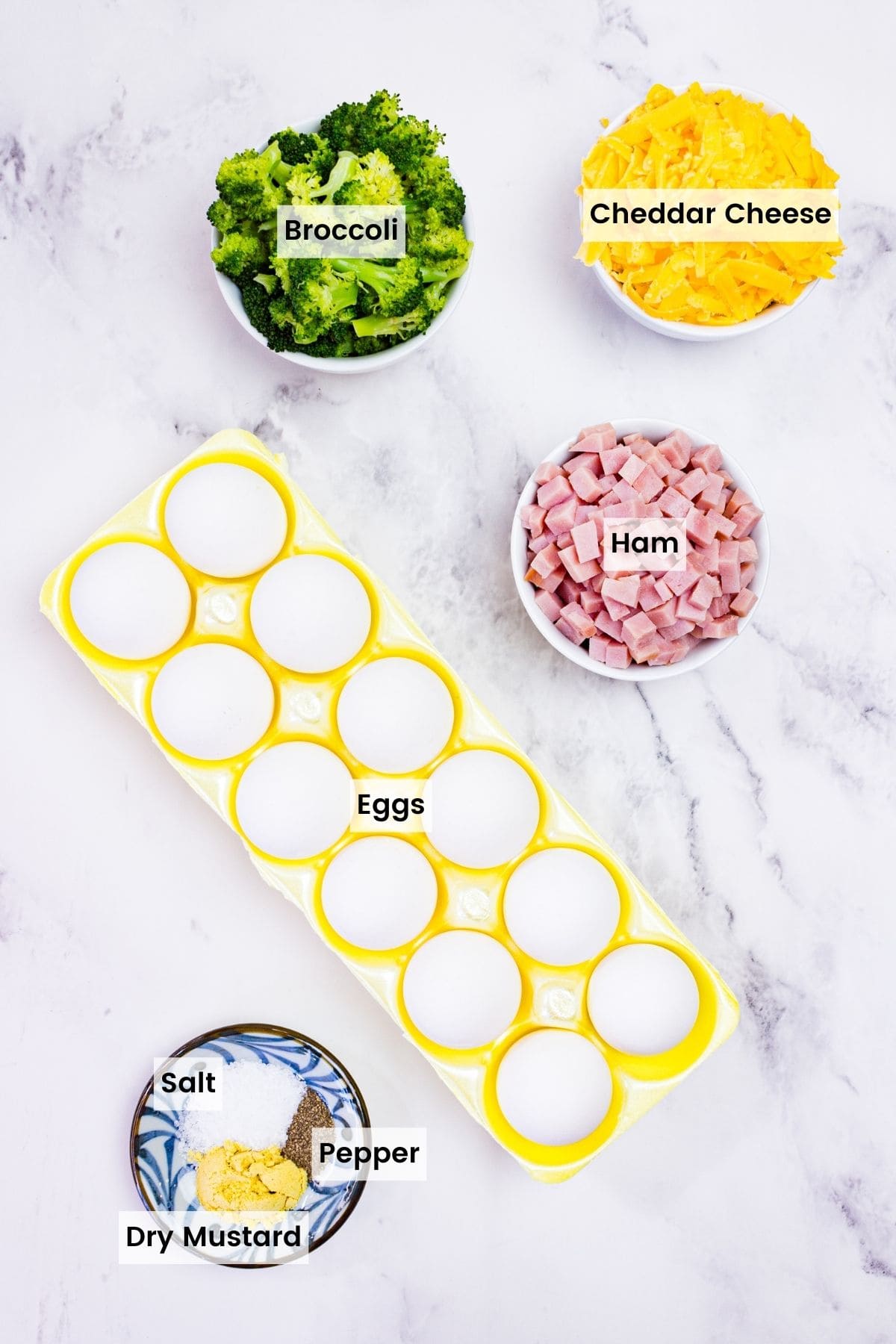 The ingredients to make broccoli, ham and cheese egg muffins on the countertop with text labels.
