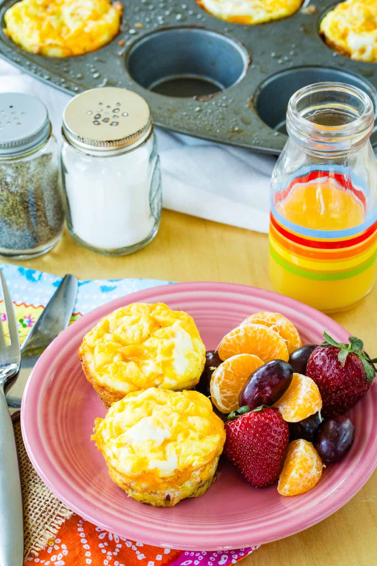 A plate of egg muffin cups and fruit next to a glass of orange juice and salt and pepper shakers.