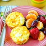 An overhead view of two egg muffins, fruit, and a fork on a pink plate.