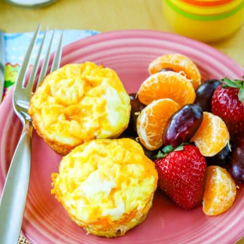 An overhead view of two egg muffins, fruit, and a fork on a pink plate.